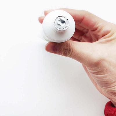 A person holding a white tube of Aloe Vera face cream with a silver cap, showcasing the product's top view.